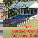 To the left Tessa on the steps holding a microphone. To the right a cricket pavilion in a park. Text: Free outdoor comedy Auckland Domain